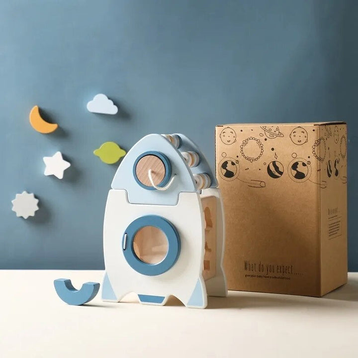 Blue and white wooden rocket activity toy beside its space-themed cardboard box.