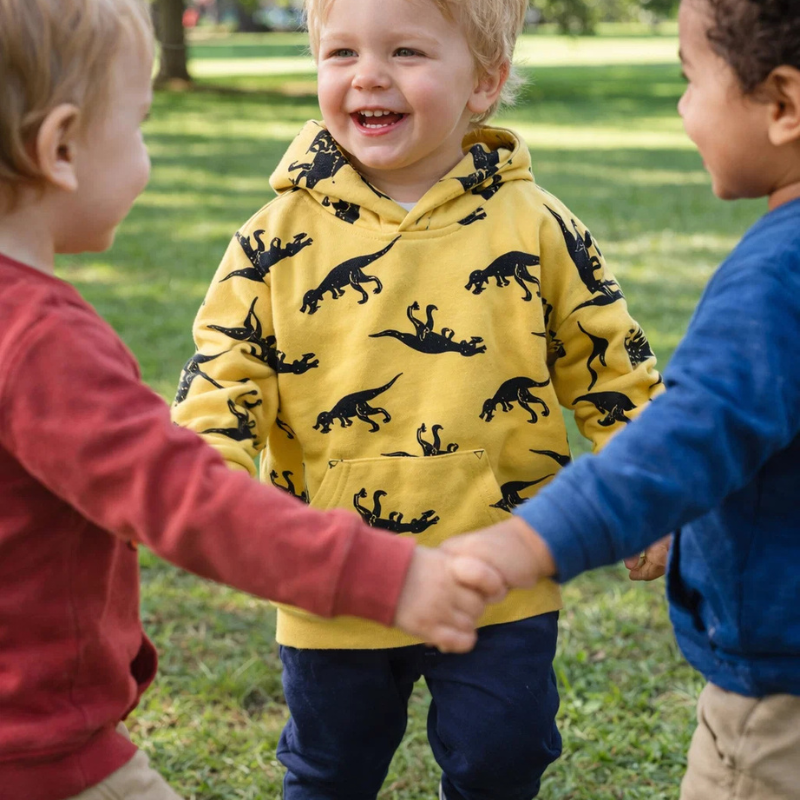 Children playing together outdoors, with one wearing a yellow dinosaur hoodie