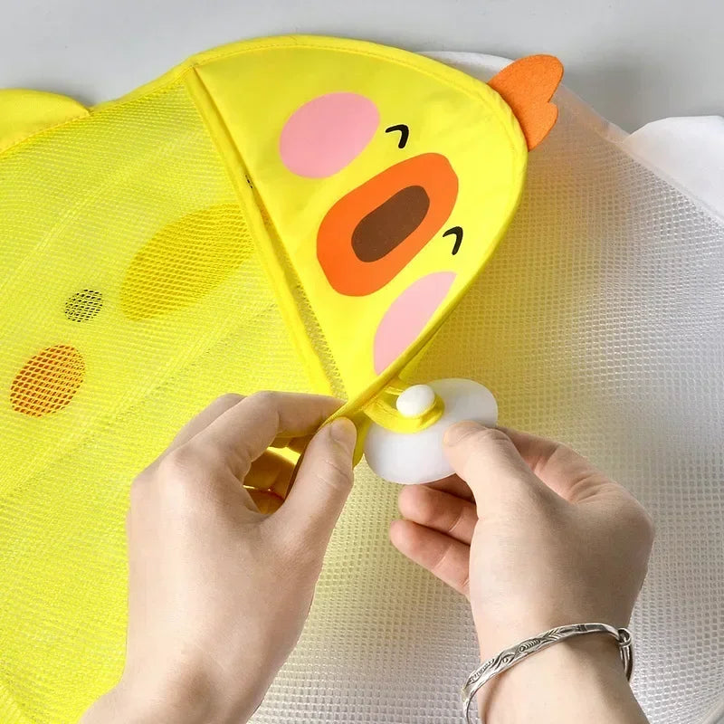 Hands attaching a suction cup to the upper corner of a yellow duck bath organizer