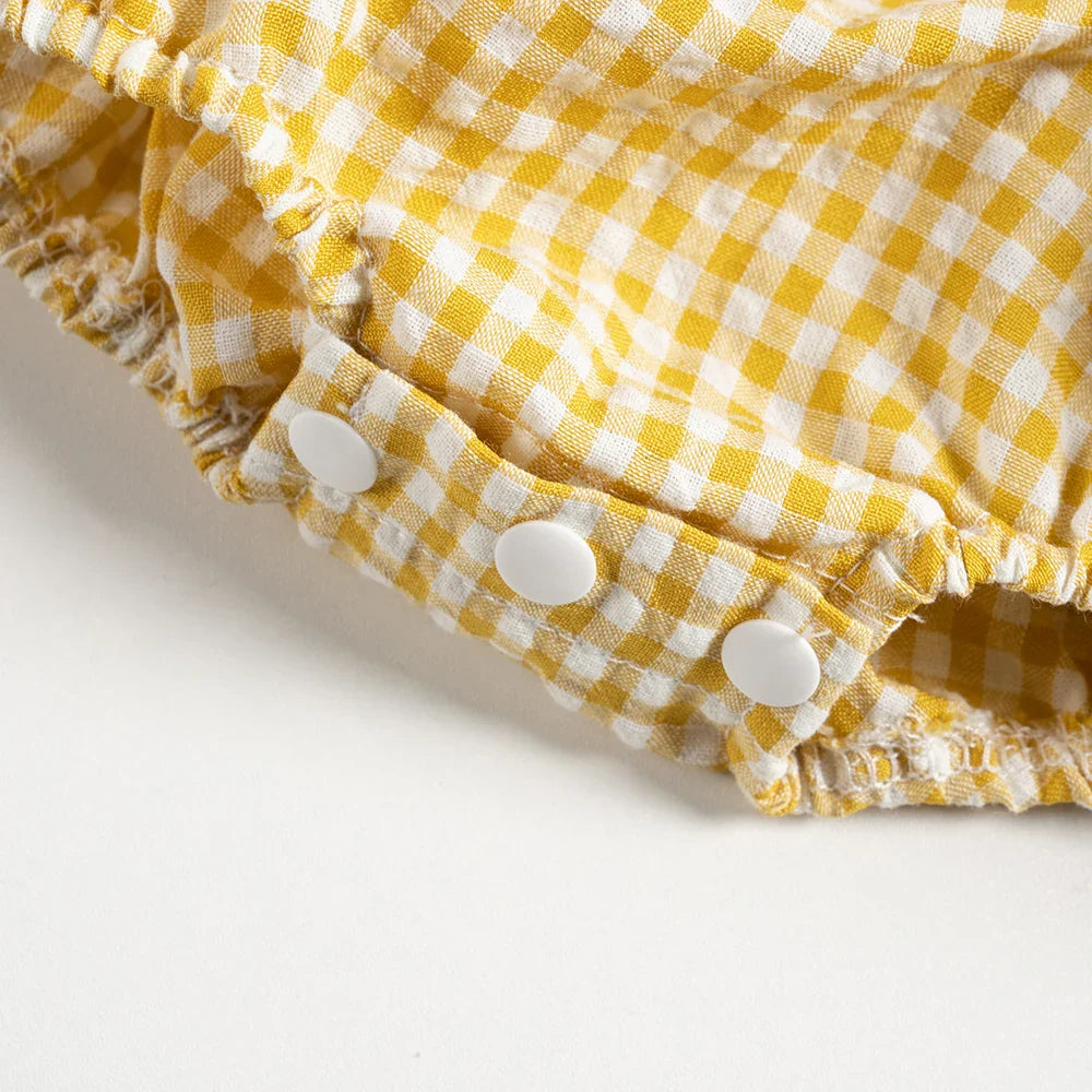 Three white snaps at the crotch of the yellow gingham baby romper