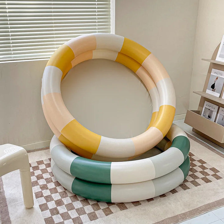 Yellow color-block inflatable pool propped above a green-and-white pool indoors.